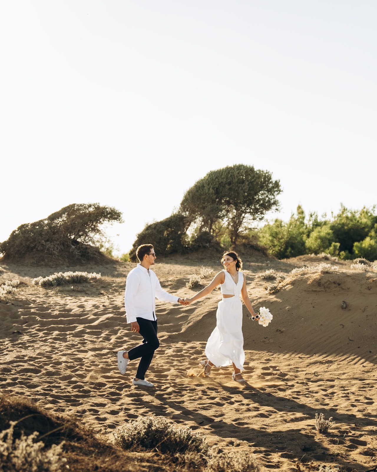 Un couple se tenant la main et souriant dans les dunes au soleil